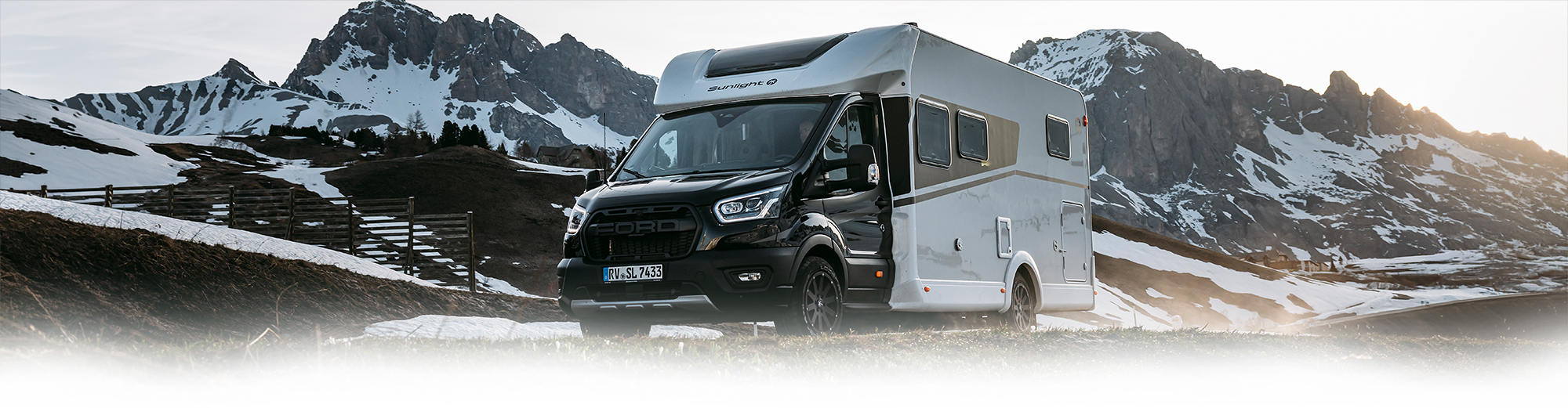 Wohnmobil mit dunklem Chassis und weißem Aufbau in einer Bergkulisse.