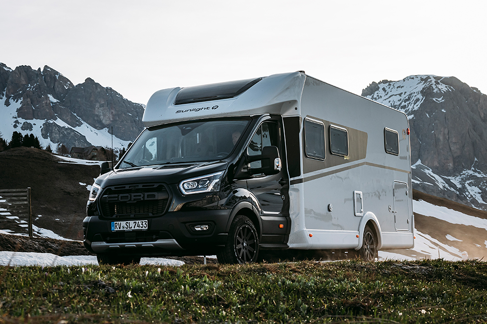 Wohnmobil mit dunklem Chassis und weißem Aufbau in einer Bergkulisse.