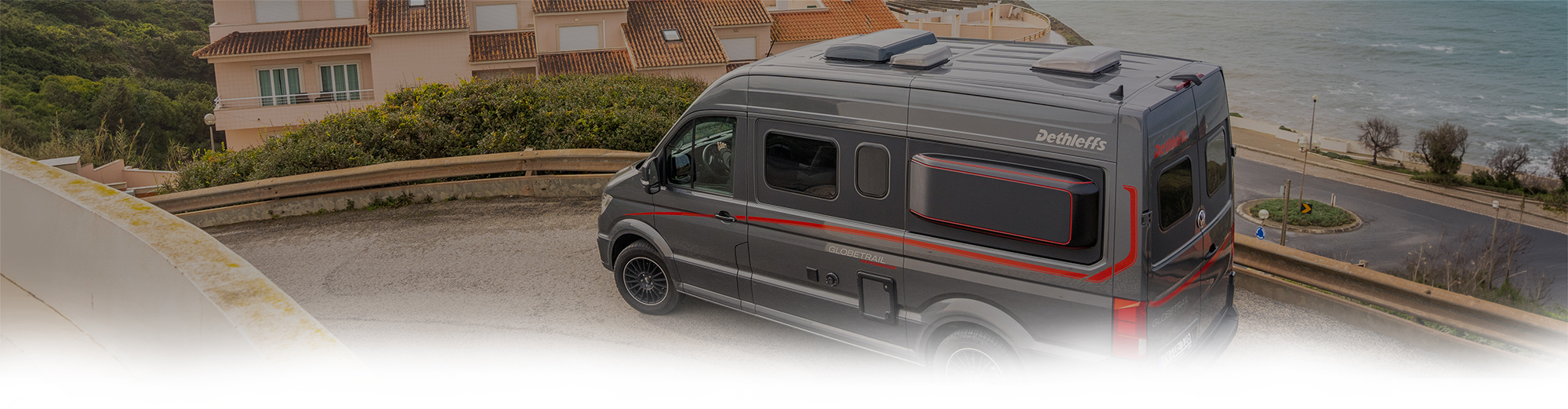 Grauer Camper Van von Dethleffs oberhalb einer Küstenstraße.