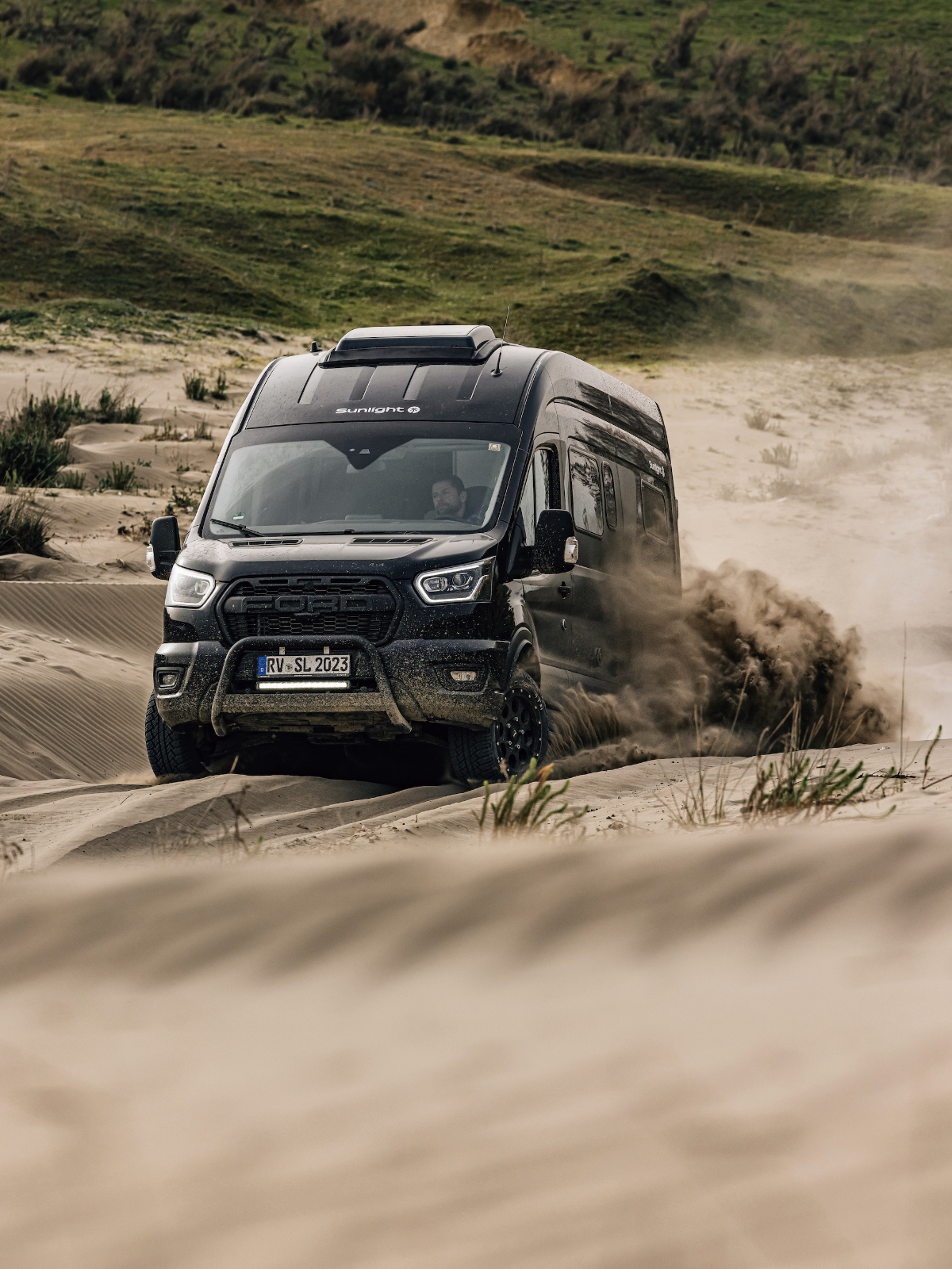 Ein schwarzer Camper Van fährt durch eine Sandlandschaft.