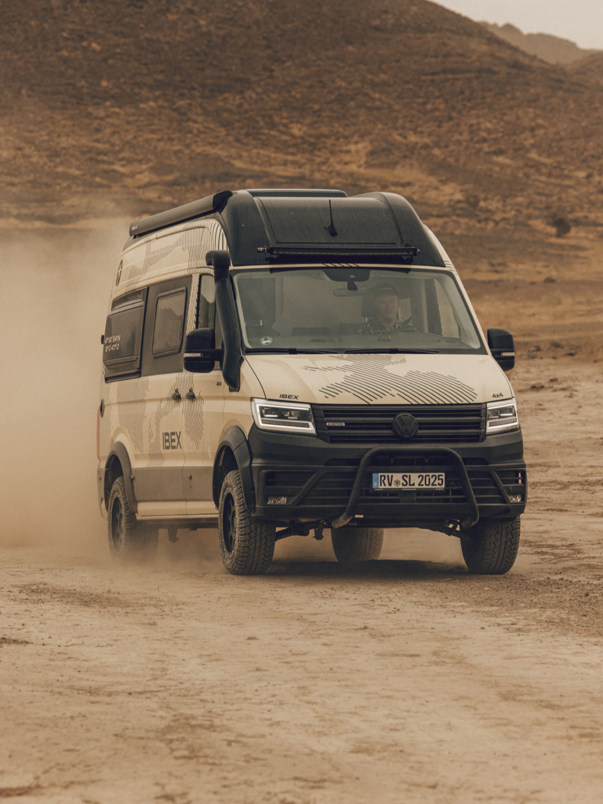 Ein weißer Camper Van fährt durch eine wüstenähnliche Landschaft.