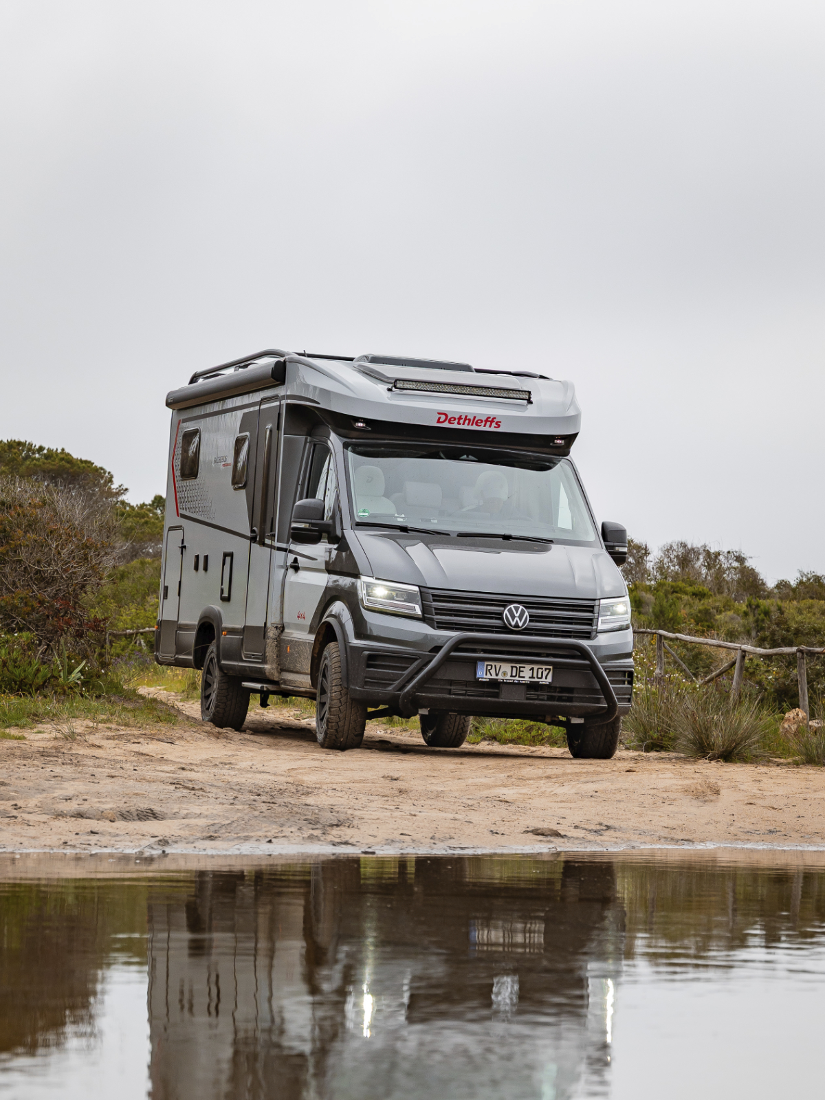 Ein graues Offroad-Wohnmobil steht vor einer Pfütze.