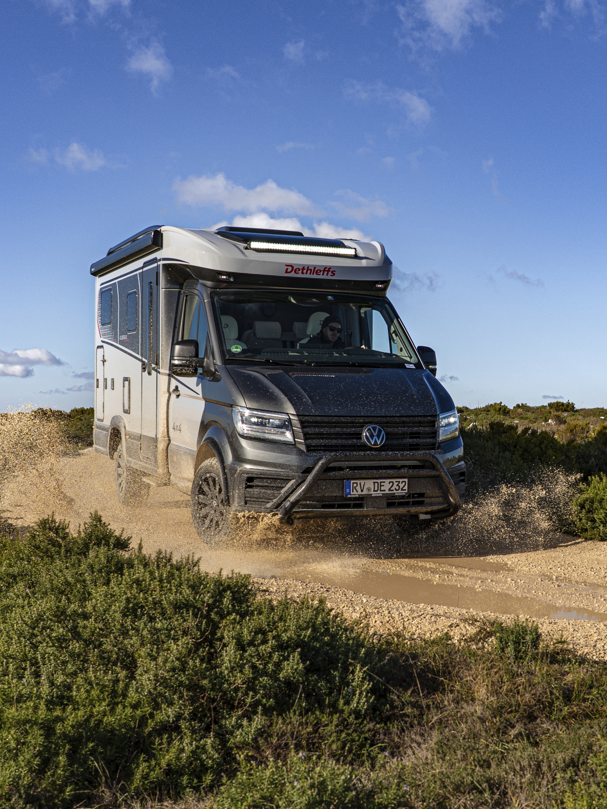 Ein helles Offroad-Wohnmobil fährt auf einem Feldweg.