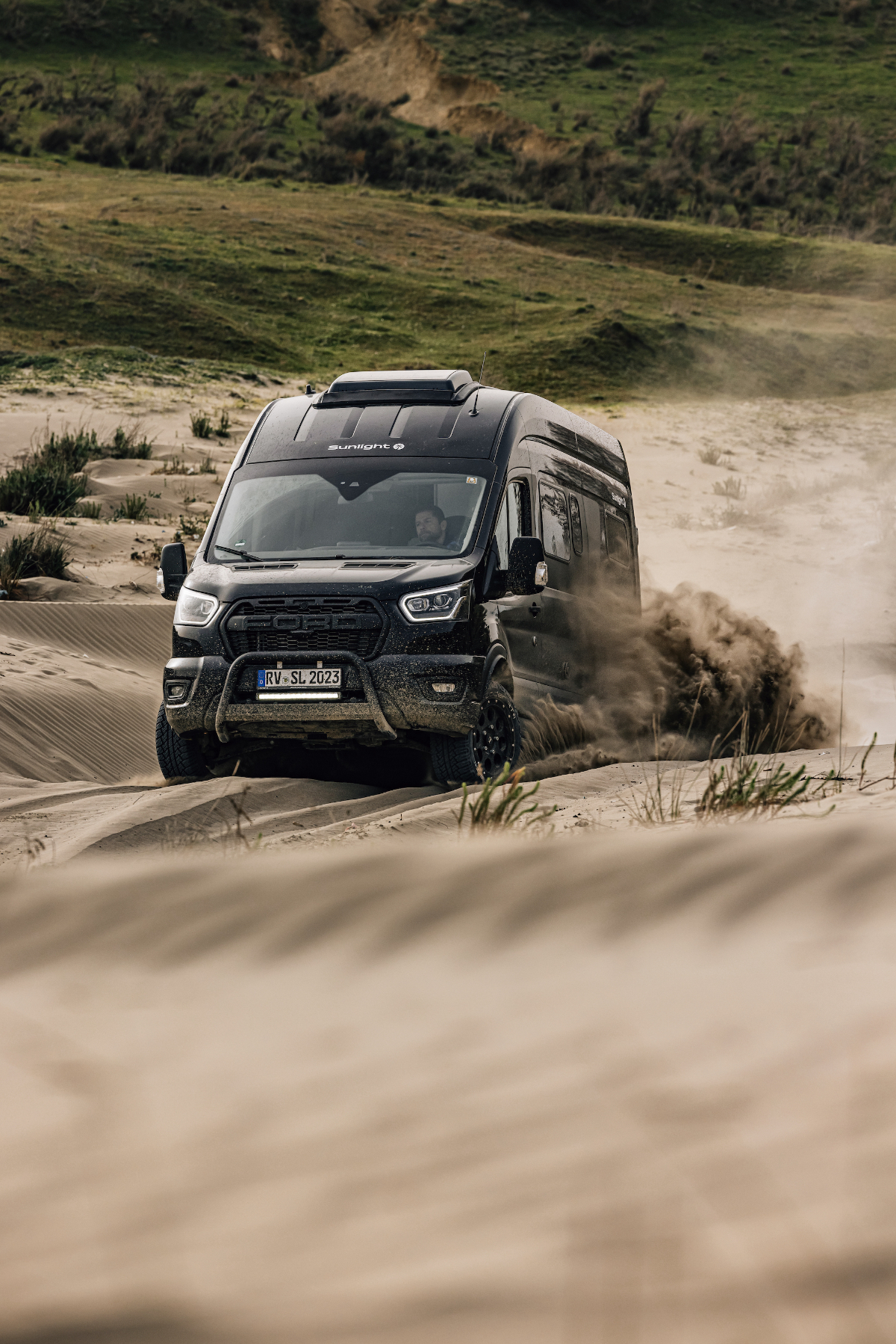Ein schwarzer Camper Van fährt durch tiefen Sand.