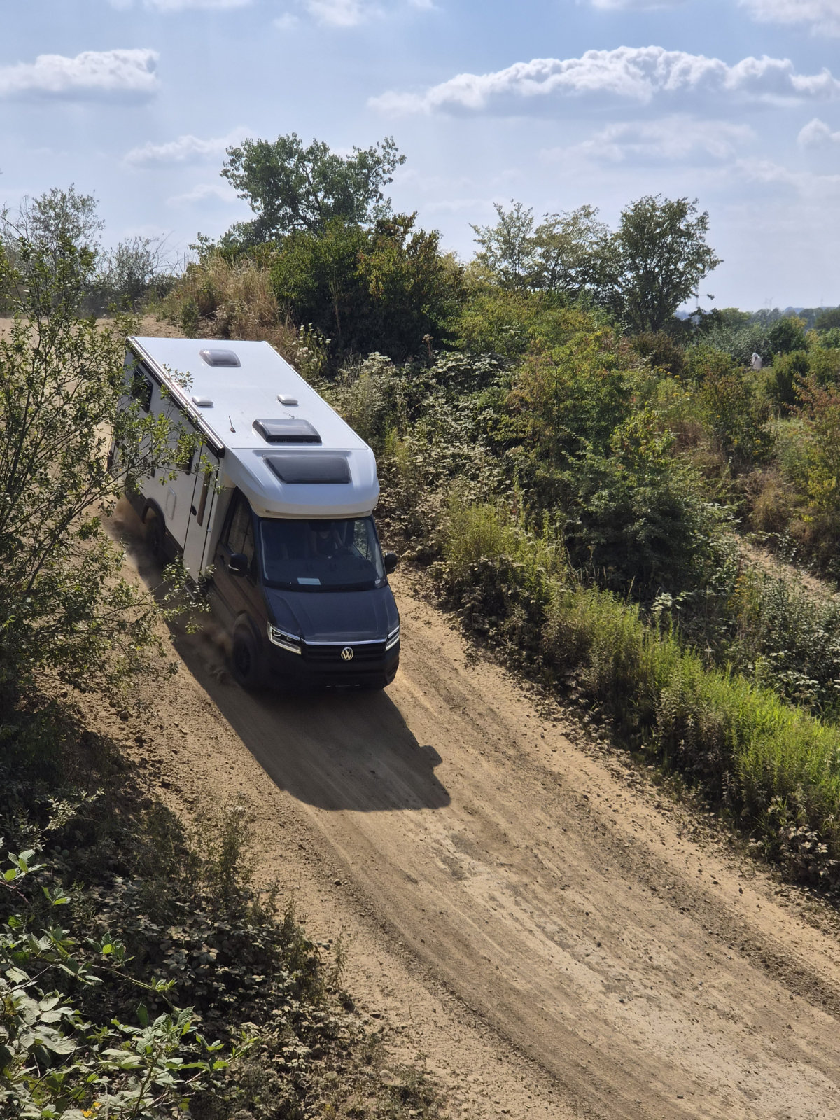 Ein weißes Wohnmobil mit dunklem Fahrerhaus fährt einen Hügel runter.