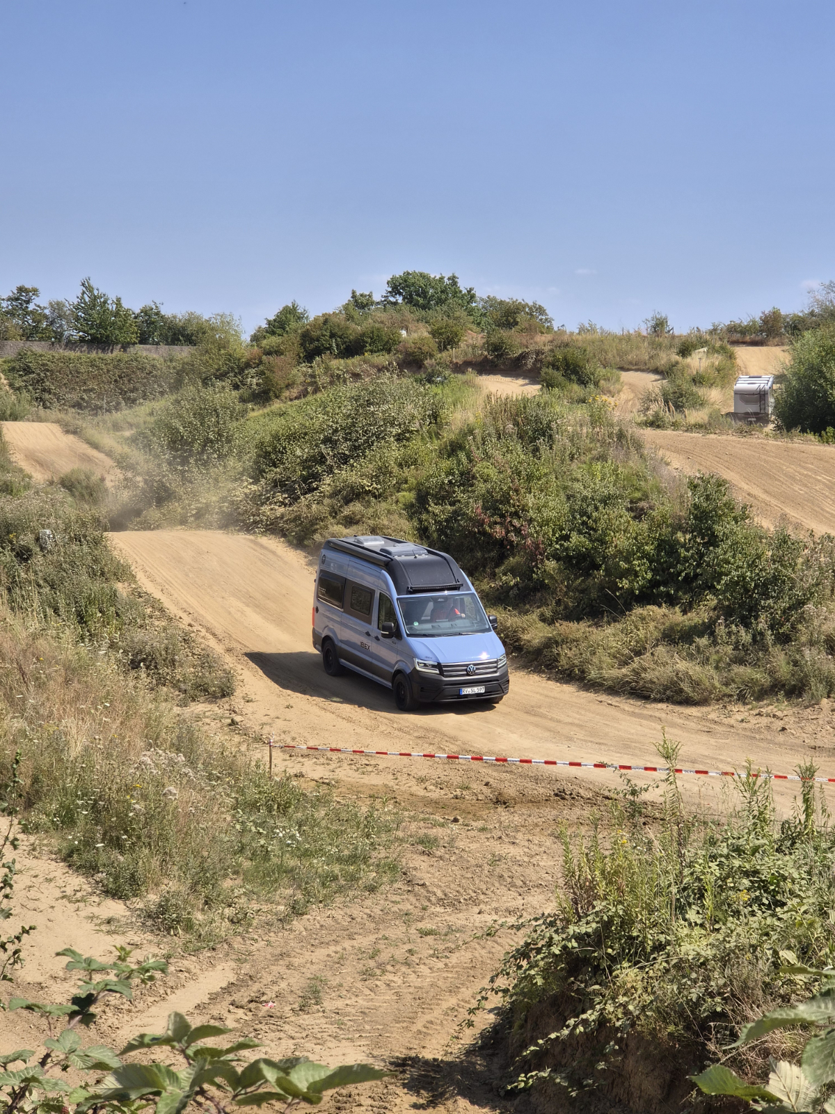 Ein blauer Camper Van fährt auf einer Geländestrecke.