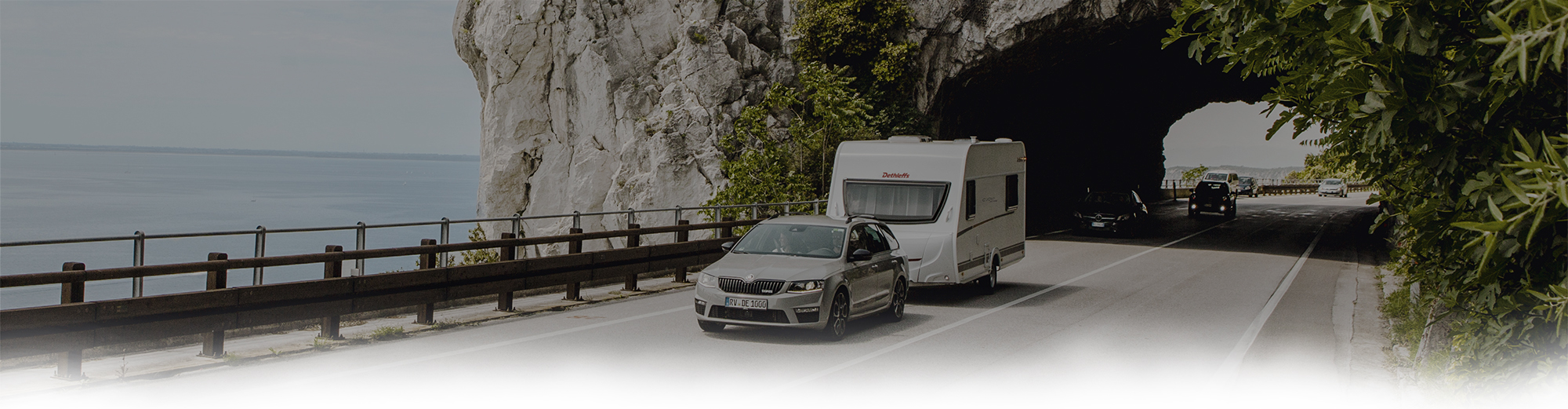 Ein Fahrzeug zieht einen Wohnwagen auf einer Küstenstraße.