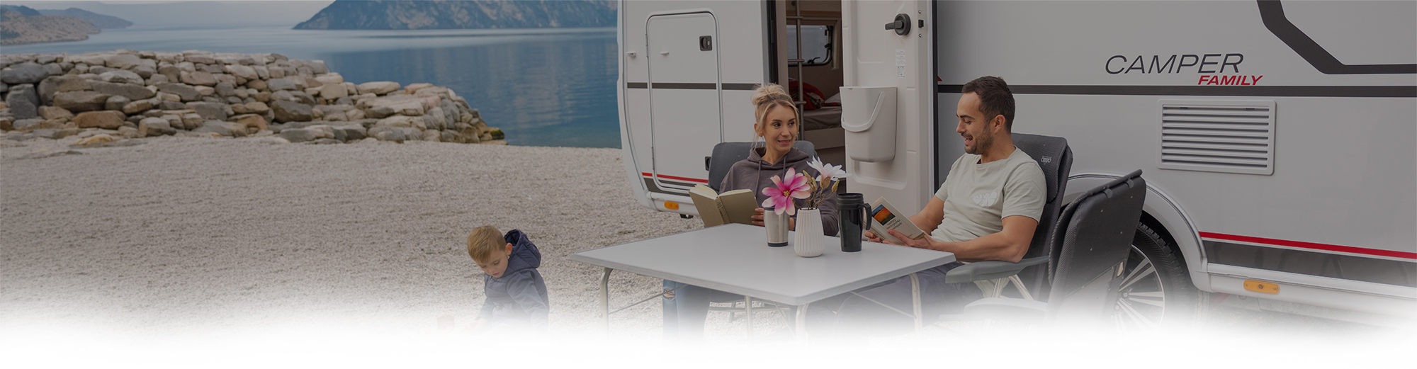 Familie mit Kind sitzt vor einem Wohnwagen.