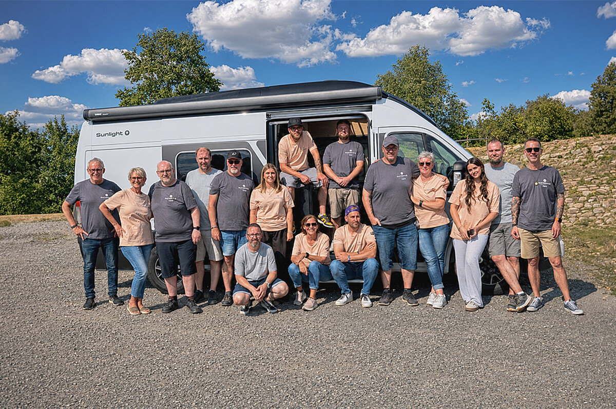 Gruppenfoto des Caravaning-Teams vor einem weißen Sunlight Campervan bei sonnigem Wetter.
