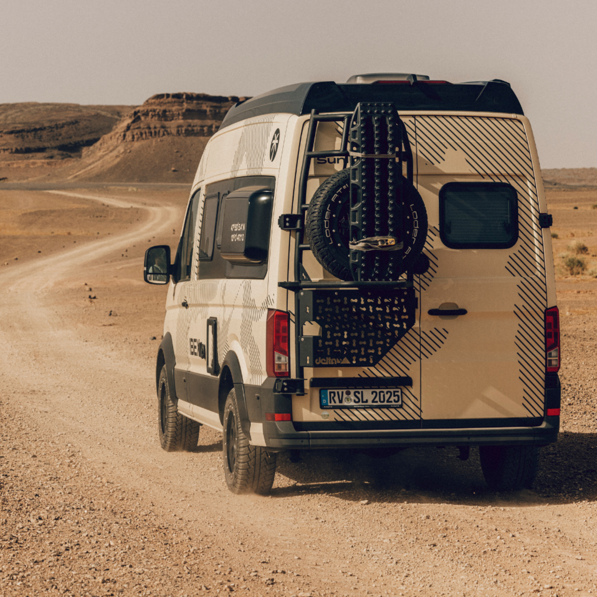 Ein heller Camper Van von hinten in einer wüstenähnlichen Umgebung.