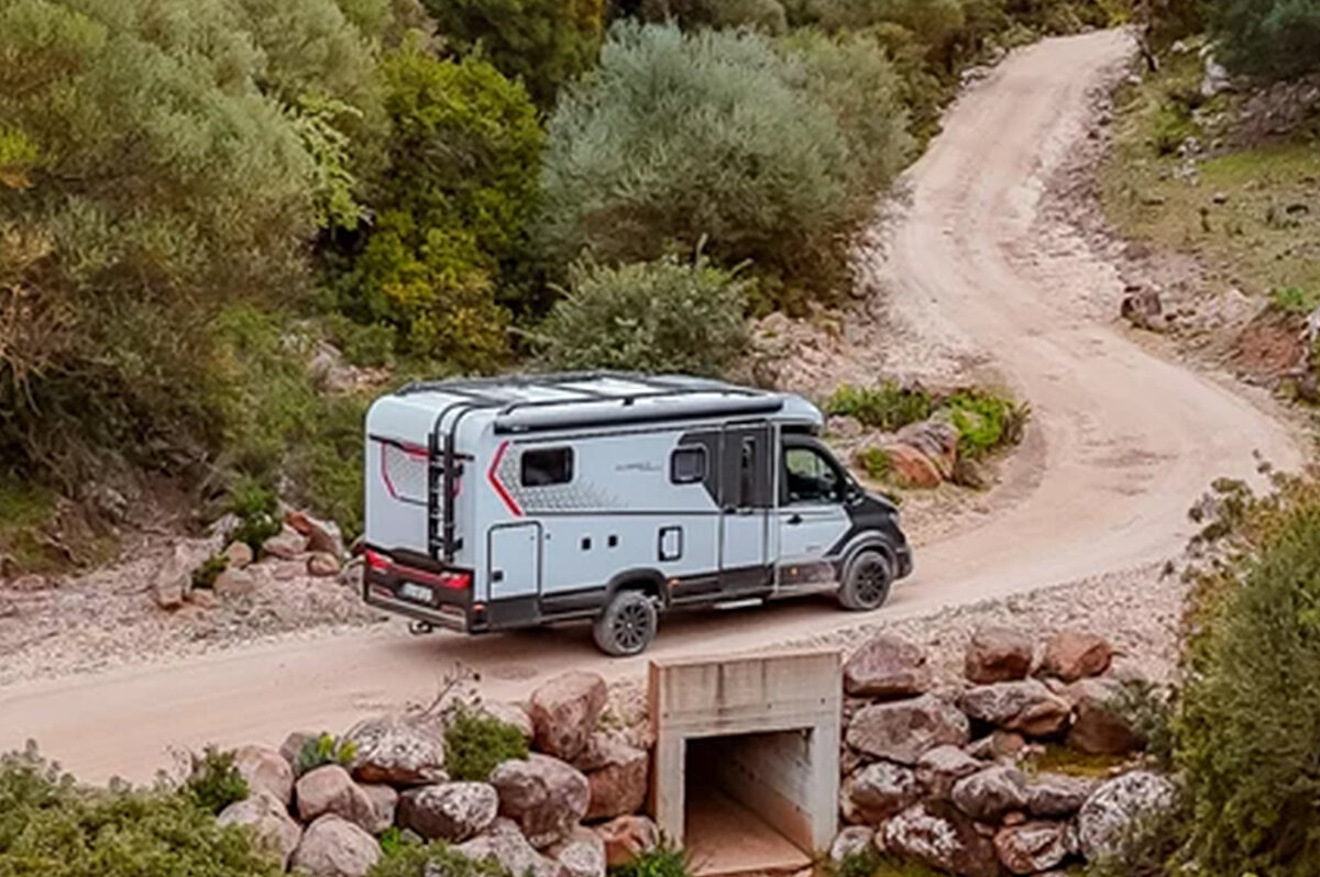 Ein weißes Wohnmobil fährt auf einem Feldweg.