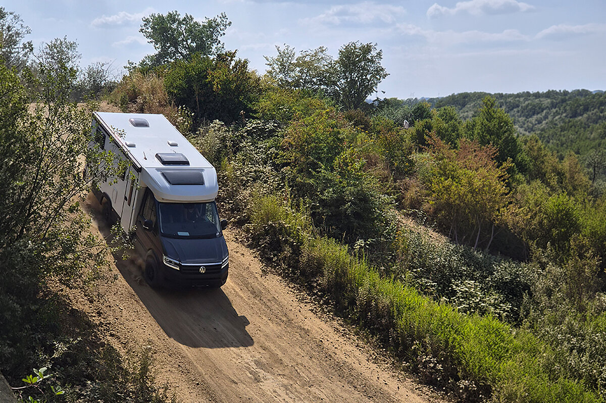 Ein weißes Wohnmobil mit dunklem Fahrerhaus fährt einen Hügel runter.