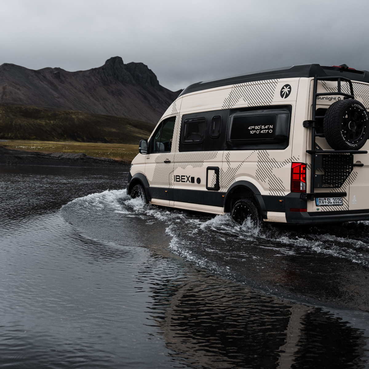 Ein heller Camper Van von Sunlight fährt durch eine Pfütze.