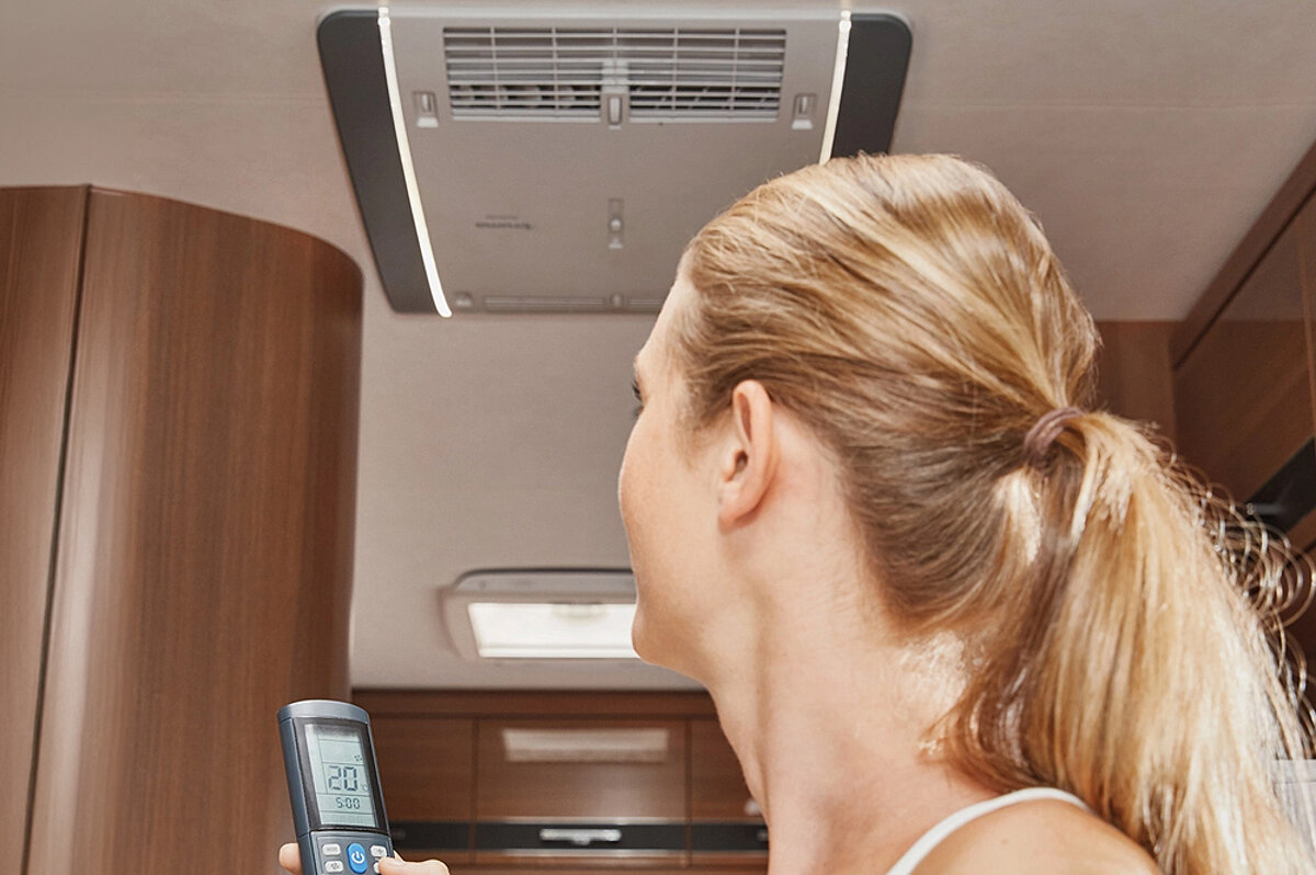 Frau mit Fernbedienung stellt Dachklimaanlage ein.