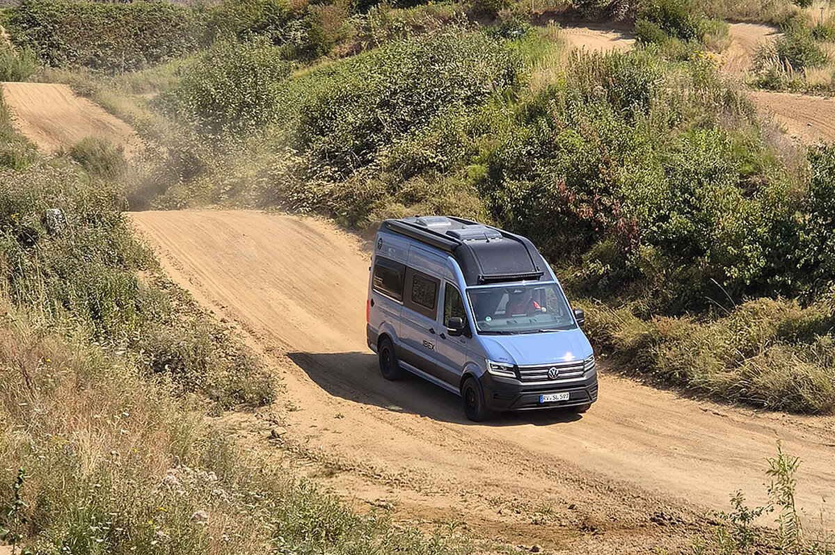 Ein blauer Camper Van fährt auf einer Geländestrecke.