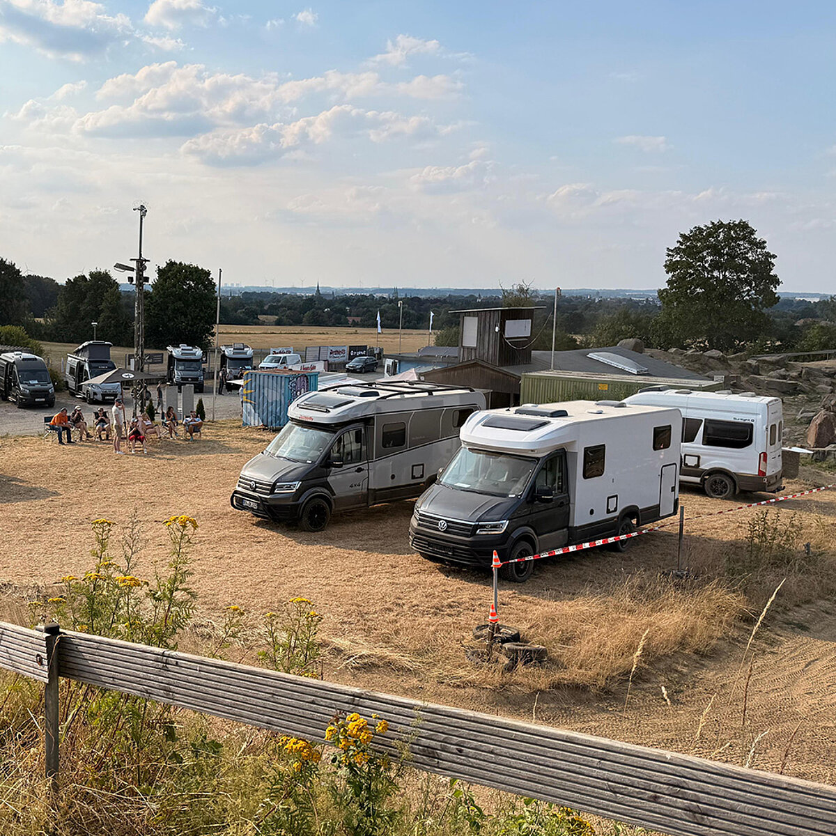 Mehrere Fahrzeuge auf einem Sandparkplatz.