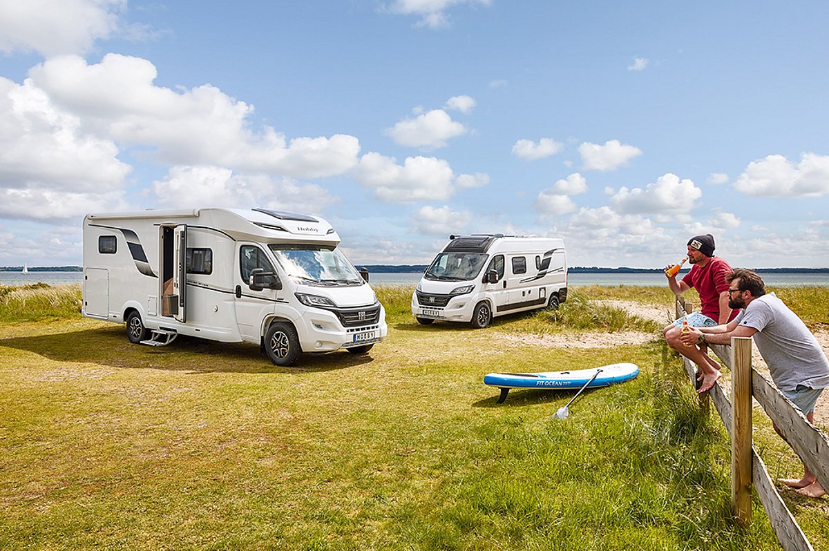 Spontan neue Naturparadiese erkunden und genießen dank der Flexibilität eines Wohnmobils. Zwei Wohnmobile auf einer Wiese. Zwei Personen befinden sich am rechten Bildrand.
