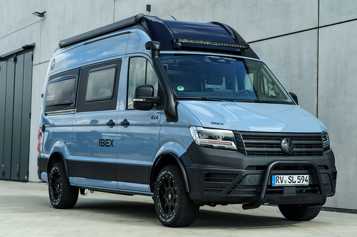 Blauer Camper Van vor einem Industriegebäude.