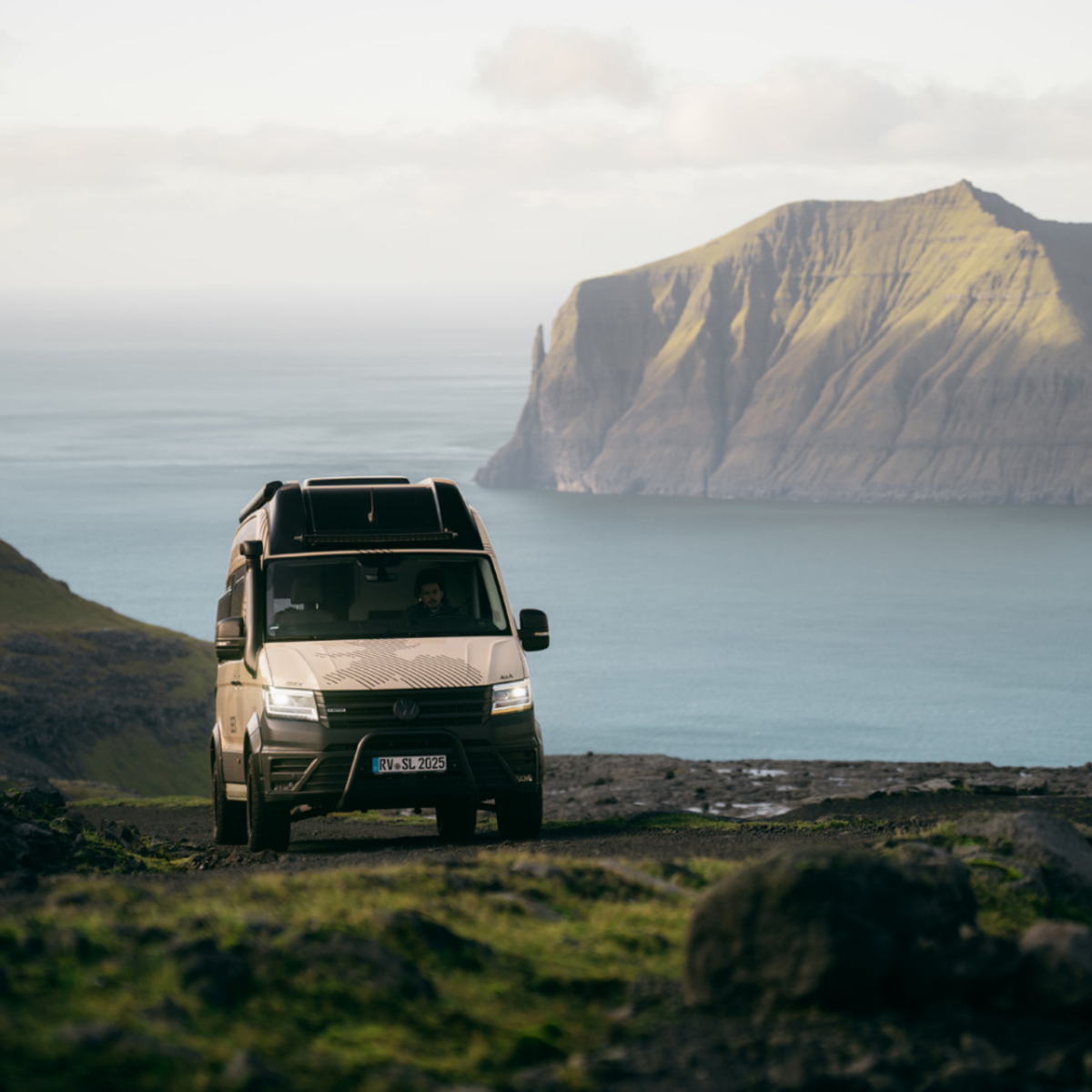 Ein heller Camper Van auf einer Wiese oberhalb einer Küste.