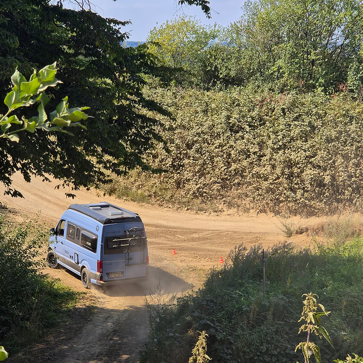 Ein blauer Camper Van auf einer Geländestrecke.