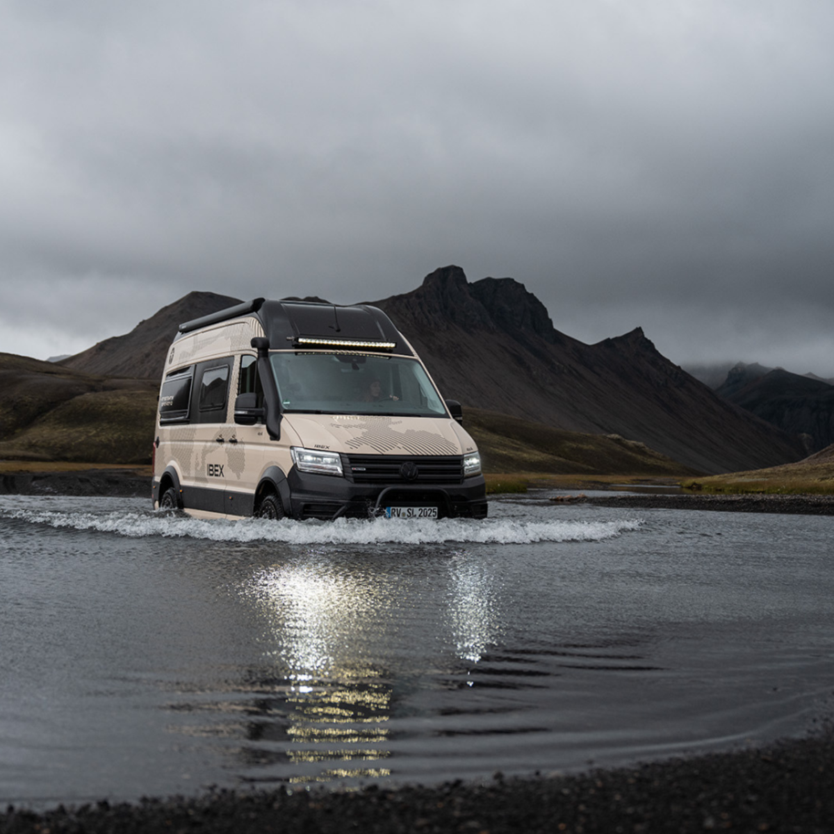 Heller Camper Van von vorne, der durch eine Pfütze fährt.