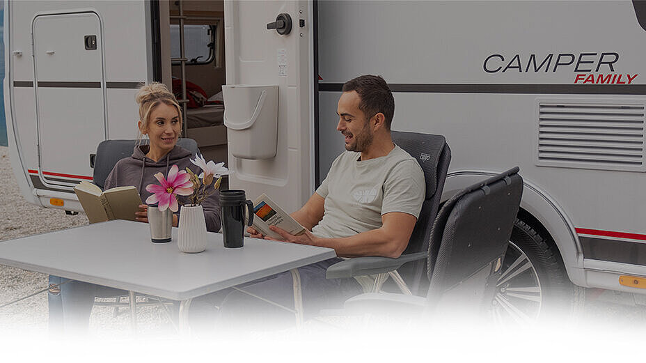 Familie mit Kind sitzt vor einem Wohnwagen.