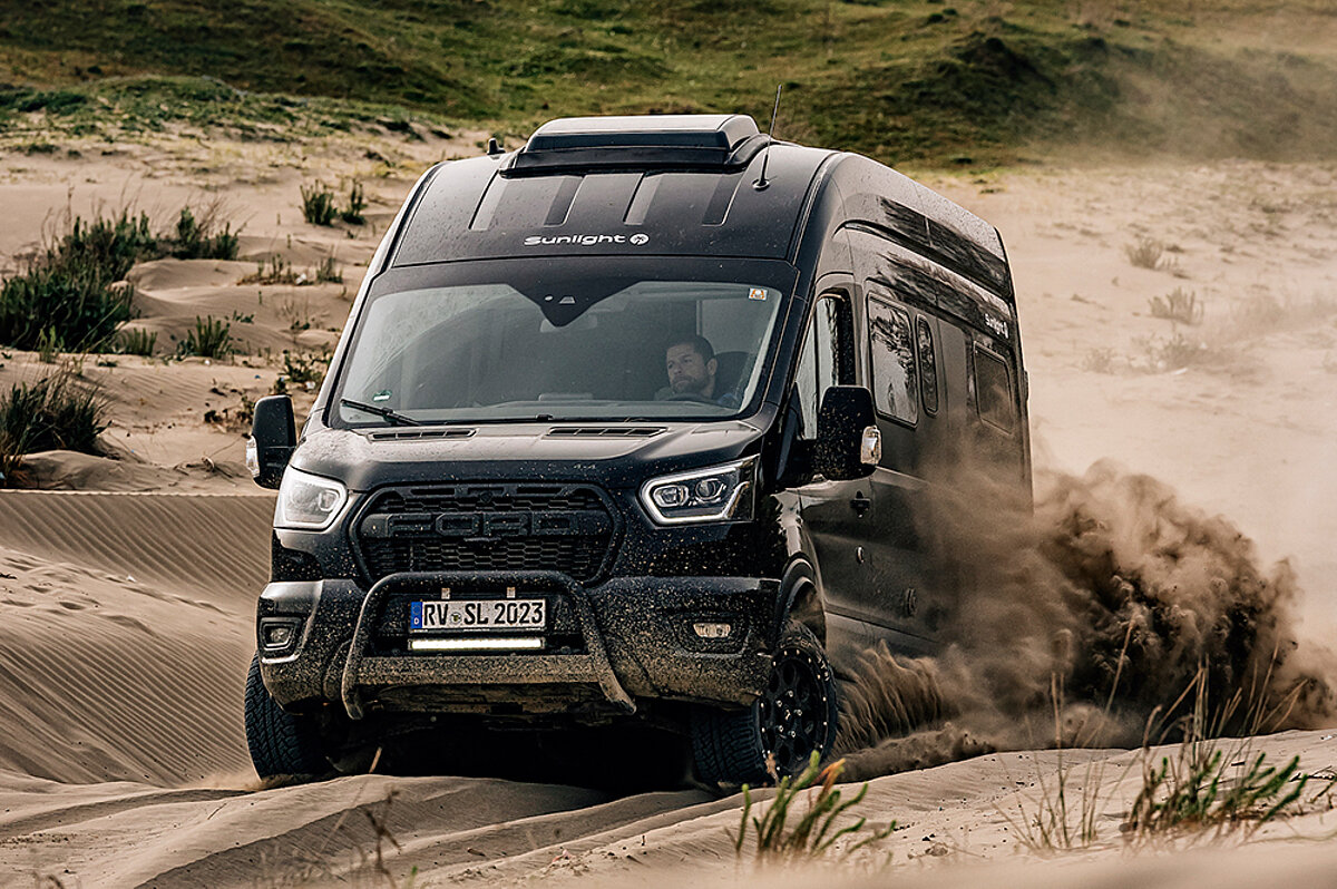 Ein schwarzer Camper Van fährt durch tiefen Sand.