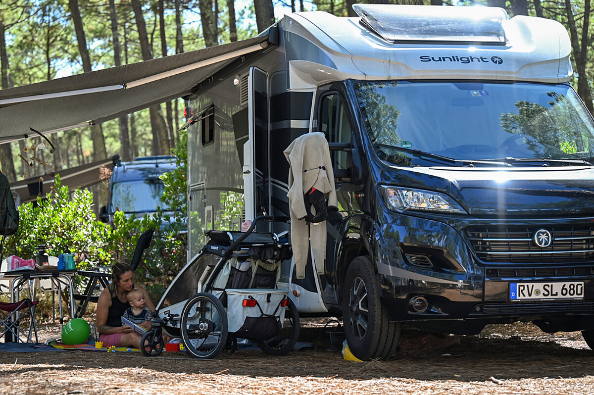 Eine Frau sitzt mit einem kleinen Kind unter dem Vordach eines Wohnmobils.